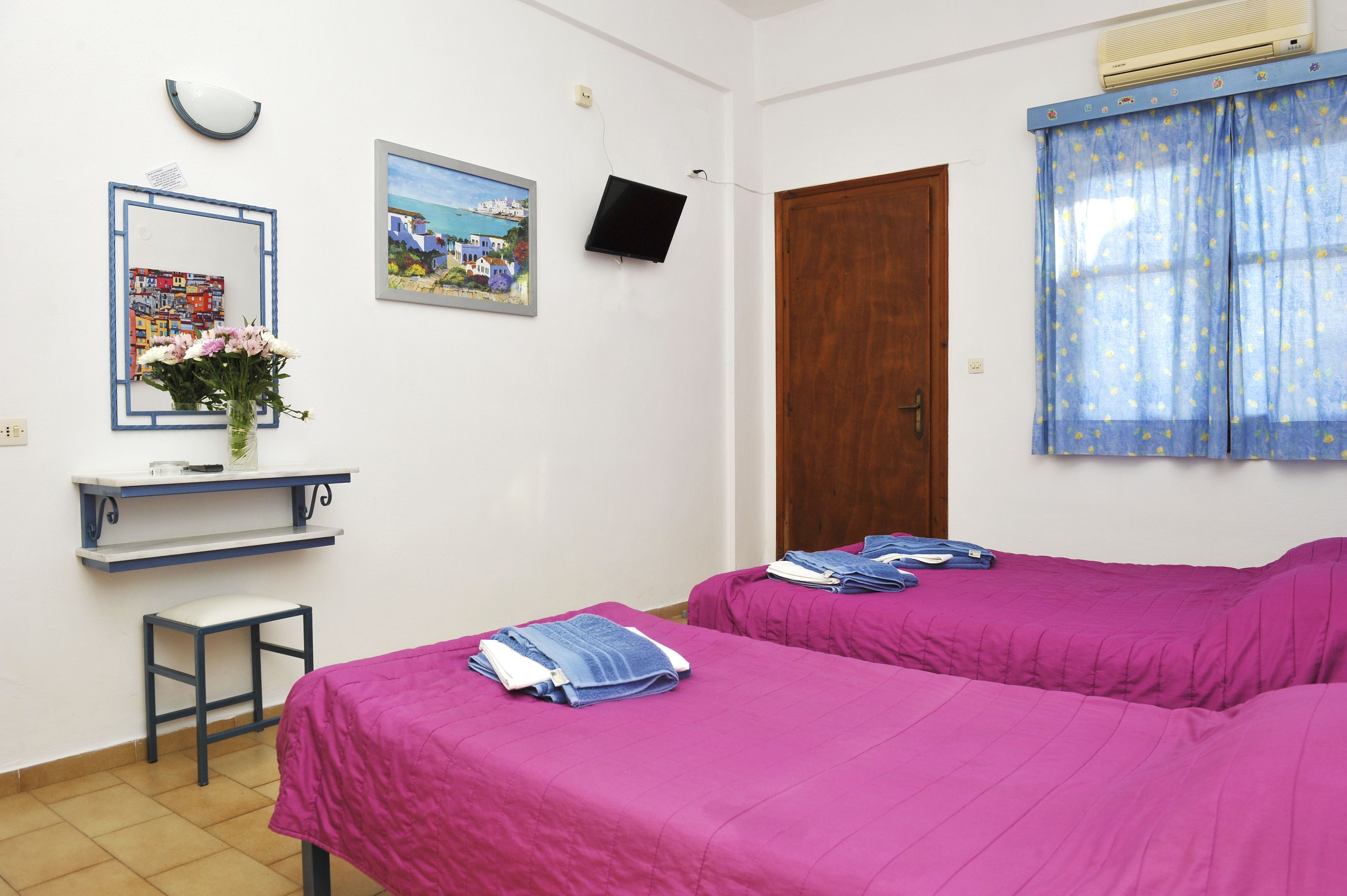 Una habitación con dos camas, un escritorio con silla, un espejo y un televisor.