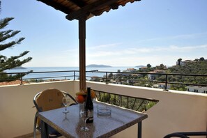 A balcony with a table set for two, overlooking a coastal view with houses and trees. - Fengeros Village (Skiathos)