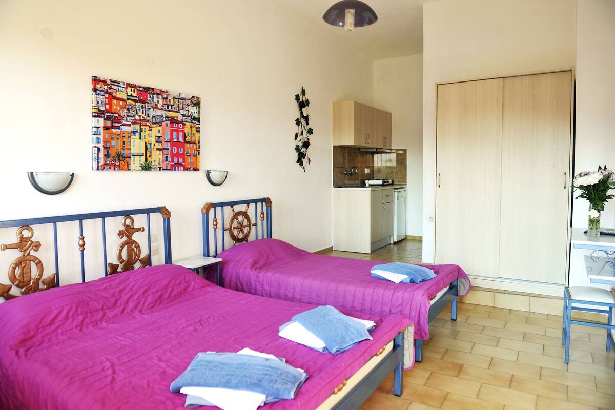 A room with two beds, a kitchenette, and a wardrobe.