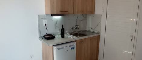A compact kitchen with wooden cabinets, a built-in dishwasher, a marble backsplash, and a white door.