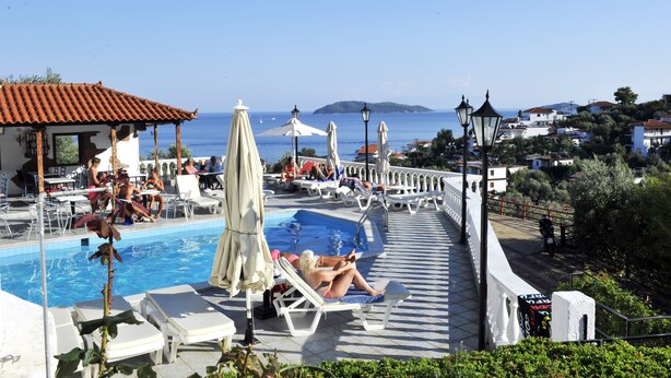 A pool area with lounge chairs and umbrellas, overlooking a coastal town. - Fengeros Village (Skiathos)