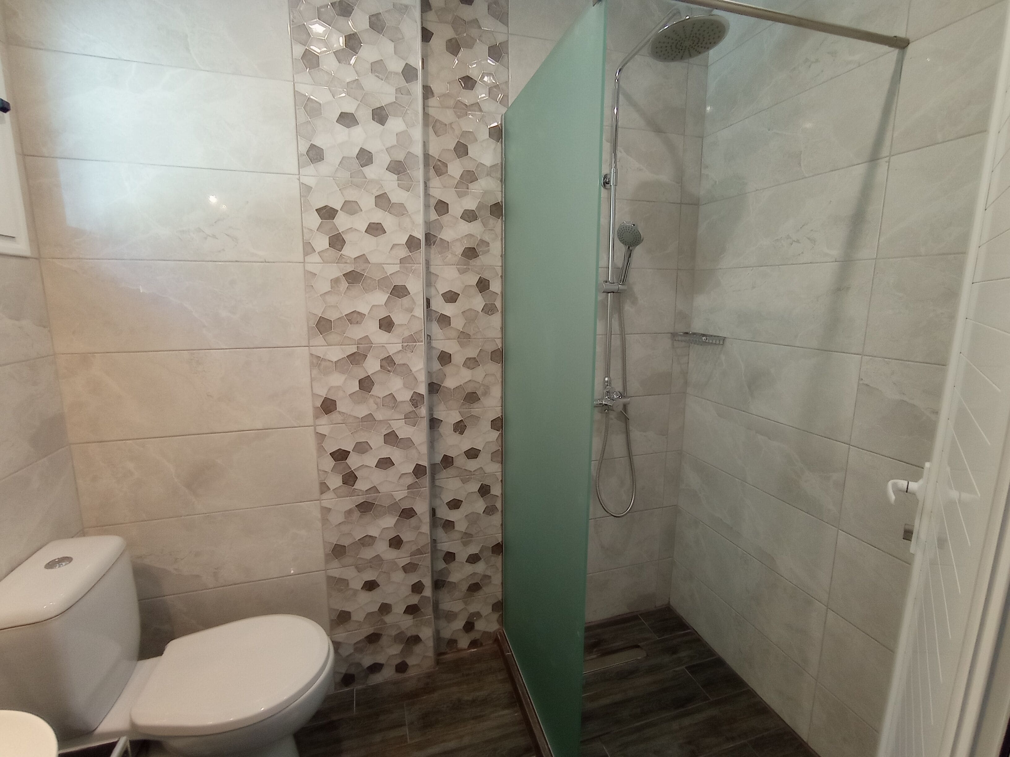 Een badkamer met een toilet, een douche met glazen deur en een betegelde muur met een geometrisch patroon.