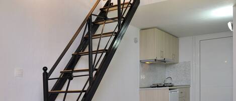 A staircase with black railings leading to a kitchen area with white cabinets and a small sink.