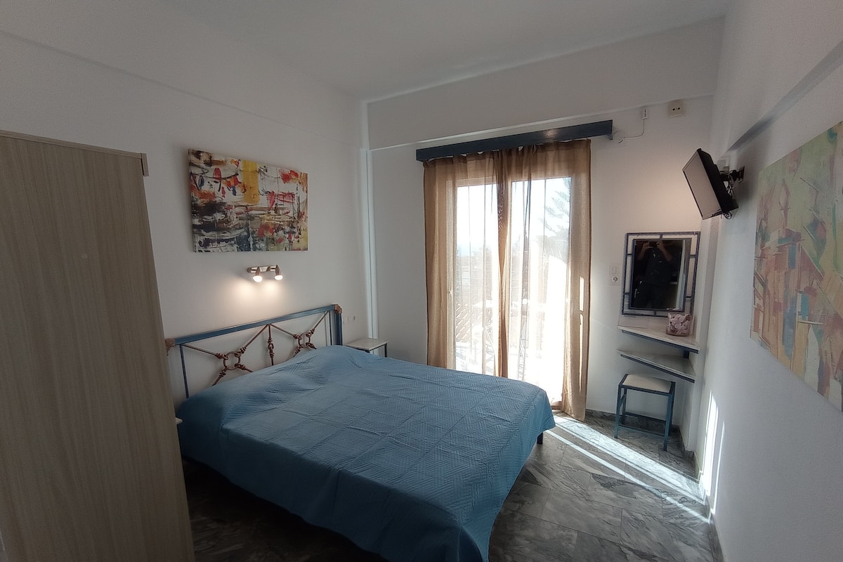 A bedroom with a bed, a desk, a TV, and a window with curtains.
