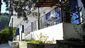 A white building with a stone wall and a balcony with blue shutters. - Fengeros Village (Skiathos)