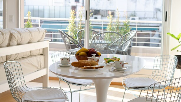 A dining area with a round table, metal chairs, a white sofa, and a balcony view. - Palermo Golf - Exclusive Apartment (Buenos Aires)
