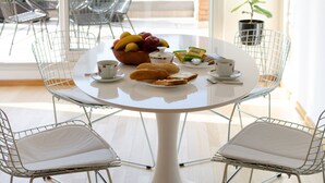 A round table with a white tablecloth, surrounded by four metal chairs with cushioned seats. A bowl of fruit, a plate of bread, and a small dish with a cup and saucer are on the table. - Palermo Golf - Exclusive Apartment (Buenos Aires)