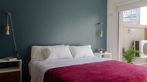 A bedroom with a bed, white bedding, a red blanket, a nightstand, a lamp, and a potted plant. - Palermo Golf - Exclusive Apartment (Buenos Aires)