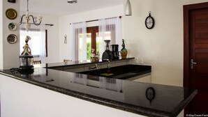 A kitchen with a central island, pendant lights, a coffee maker, and decorative items on the counter. - Pipa Casa Eduardo (Tibau do Sul)
