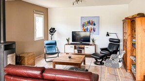 Een woonkamer met een bank, een televisie, een stoel, een tafel en een boekenkast.
