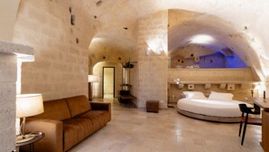A cozy, stone-walled room with a bed, a sofa, and a small table with a lamp. - BV QUARRY MATERA  (Matera)