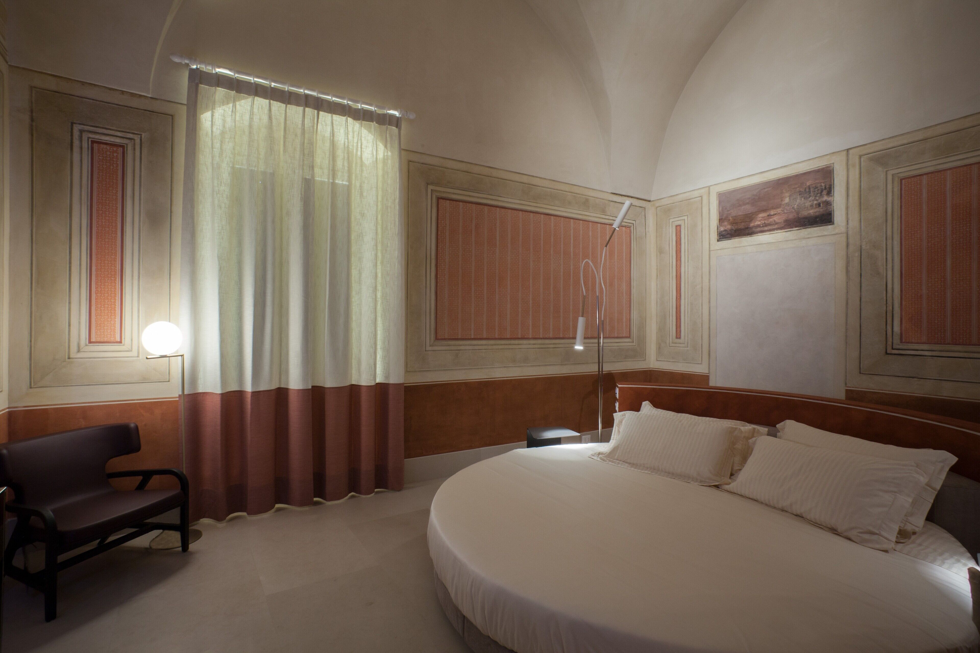 Una habitación de hotel con una cama grande, una silla, un escritorio y una ventana con cortinas.