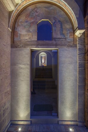 Una entrada de piedra con puerta de cristal, una escalera que da al interior y un mural en la parte superior.