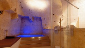 A spa room with a heated stone bath, a glass shower enclosure, and a wooden bench. - BV QUARRY MATERA  (Matera)