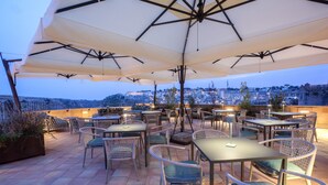 An outdoor patio with tables and chairs, umbrellas, and a view of a cityscape. - BV QUARRY MATERA  (Matera)