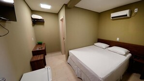 A hotel room with a bed, bedside table, a small desk with a chair, a TV mounted on the wall, and an air conditioning unit. - Wanna Hotel (Lins)