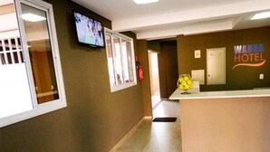 A hotel reception area with a reception desk, a television mounted on the wall, and a sign that reads "WANNA HOTEL". - Wanna Hotel (Lins)