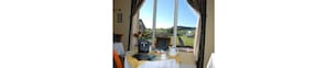 Una habitación con una mesa dispuesta para el desayuno, vistas al campo y una ventana con cortinas.