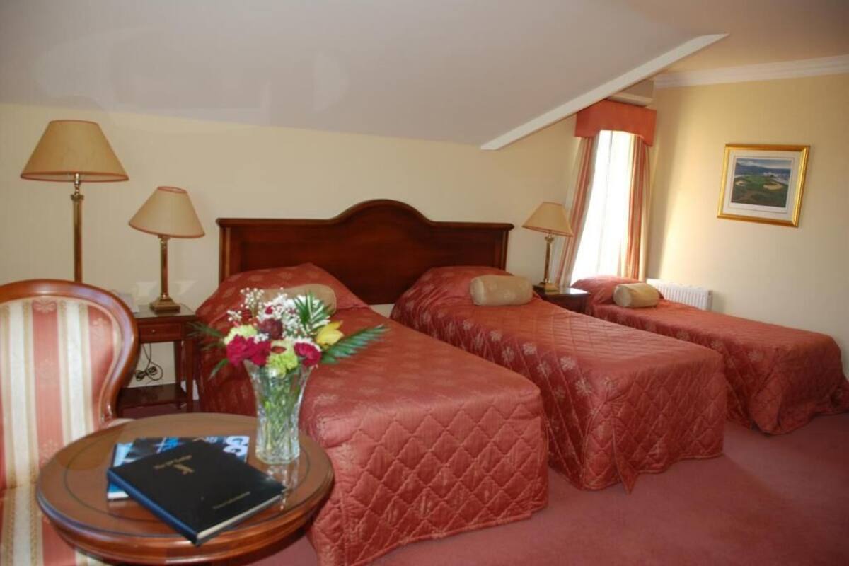 A hotel room with two single beds, a wooden chair, a small table with a book and a vase of flowers, and two bedside lamps.