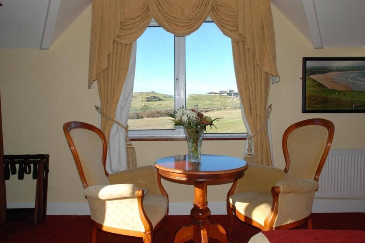 A room with a large window, two wooden chairs, a round wooden table, and a vase with flowers.