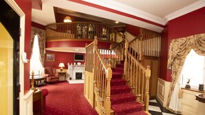A grand staircase with wooden balusters and red carpeted steps leading to a second floor. - The 19th Lodge Ballybunion (Ballybunion)