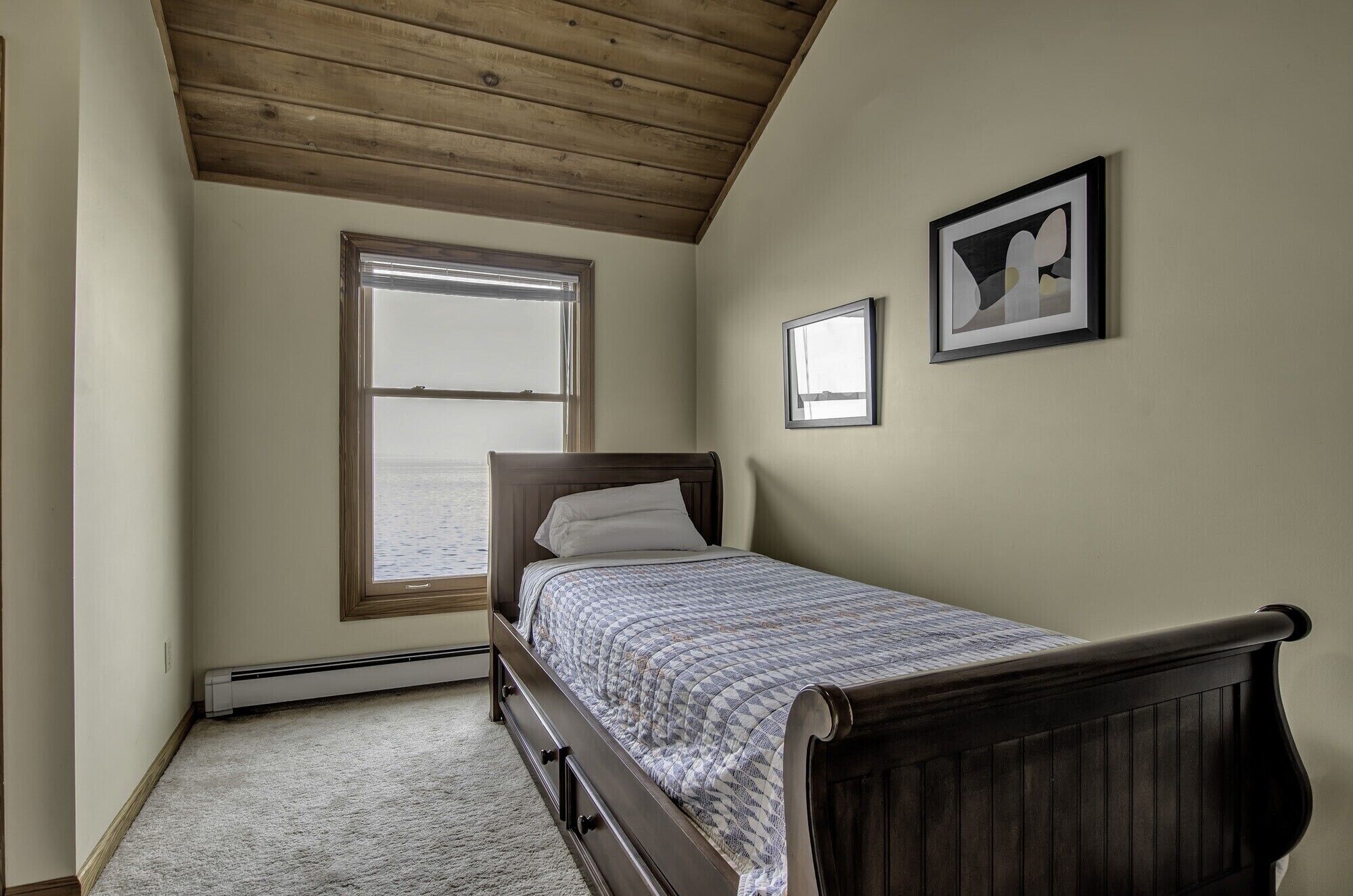 Une chambre avec un plafond en bois, un lit recouvert d’une couvre-lit à motifs, une fenêtre donnant sur un beau paysage et un tableau encadré accroché au mur.