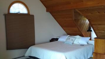 A bedroom with a sloped ceiling, a bed with white bedding, a wooden headboard, a nightstand, a desk, and a ceiling fan.