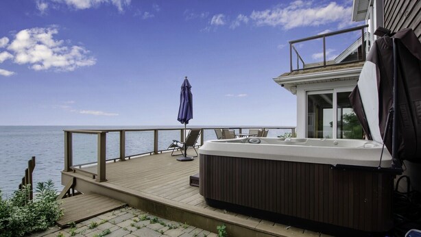 A deck with a hot tub, lounge chairs, and a view of the sea.