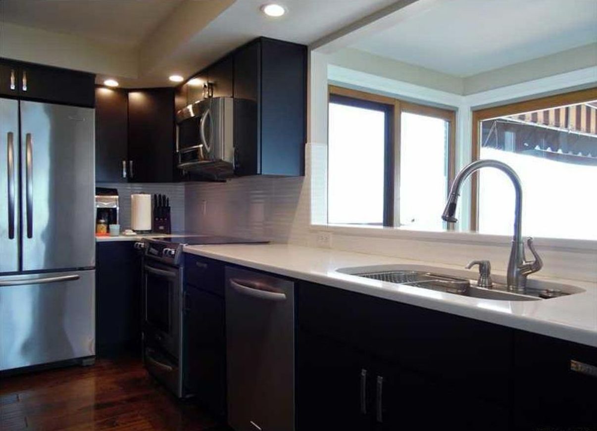 A modern kitchen with stainless steel appliances, a dishwasher, and a large window providing natural light.