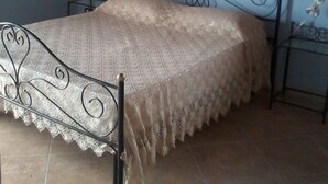A bed with a metal frame and a lace bedspread in a room with blue walls and tiled flooring. - Batarà B&B (Agrigento)