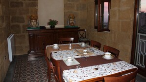 A dining area with a stone wall, a wooden table set with plates, cups, and cutlery, and a window with a view. - Batarà B&B (Agrigento)