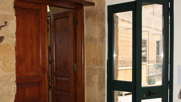A hallway with a wooden door and a glass door leading to an outdoor area. - Batarà B&B (Agrigento)