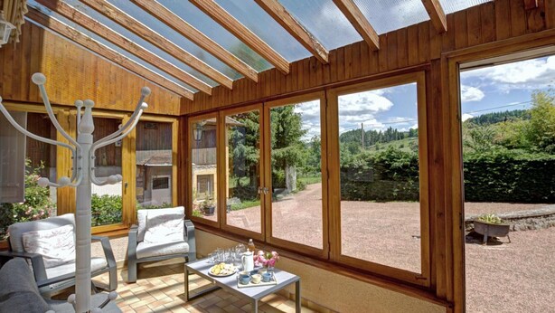 A sunlit room with wooden walls and large windows, a table with breakfast items, and a view of a rural landscape.