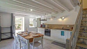 A spacious kitchen with white cabinetry, a wooden dining table, and white chairs. There is a staircase with patterned tiles leading to another level.