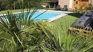 A swimming pool surrounded by a well-maintained lawn, stone building, and outdoor seating area.