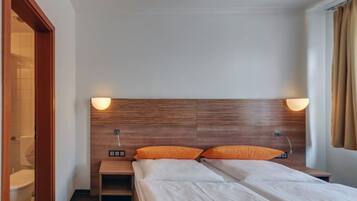 Habitación de hotel con cabecera de madera, dos almohadas, una mesita de noche y una ventana con cortinas.