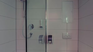 A modern bathroom with a glass shower enclosure, a towel dispenser, and a soap dispenser on the wall. - Hotel Drei Kaiserberge (Goeppingen)