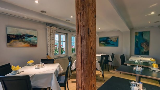 A dining area with tables set for two, a wooden column, and artwork on the walls. - Hotel Drei Kaiserberge (Goeppingen)