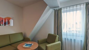A modern hotel room with a green sofa, a small round table, and a large window with sheer curtains. - Hotel Drei Kaiserberge (Goeppingen)