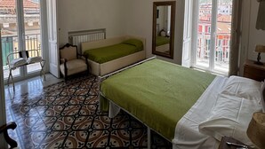Une chambre à coucher avec un lit, une chaise, un miroir et une fenêtre donnant sur des immeubles.