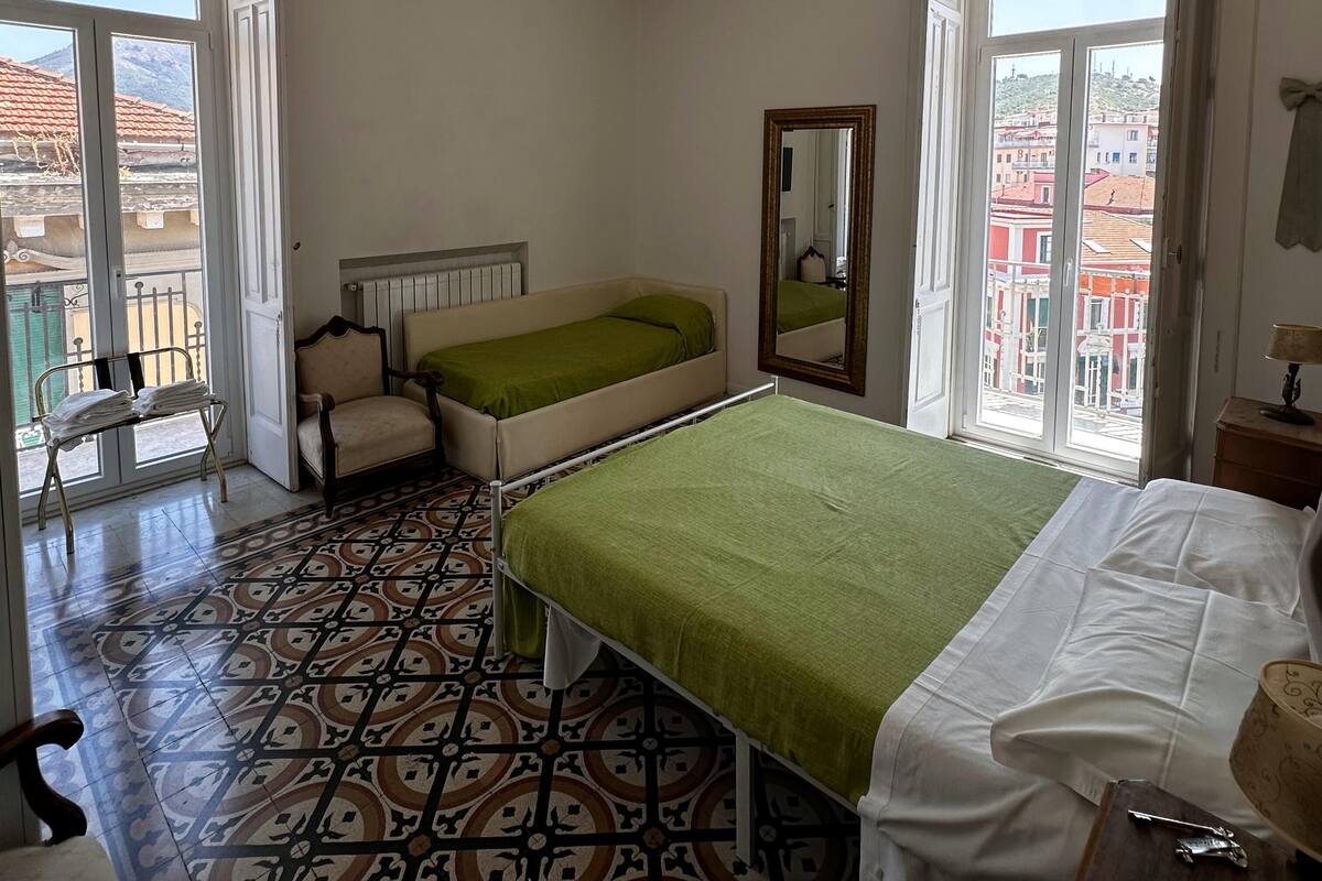 A bedroom with a bed, a chair, a mirror, and a window with a view of buildings.