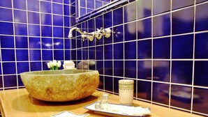 Une salle de bain avec un grand lavabo en pierre, une petite bougie blanche et une assiette décorative posée sur un comptoir en bois.