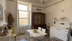 Un coin repas avec une table et des chaises blanches, un sol à motifs, un meuble en bois et une fenêtre donnant sur un paysage agréable.