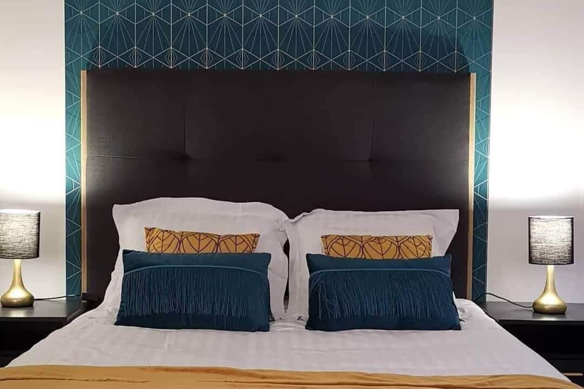 Un lit avec une tête de lit sombre, deux lampes de chevet et un mur orné d’un motif géométrique.