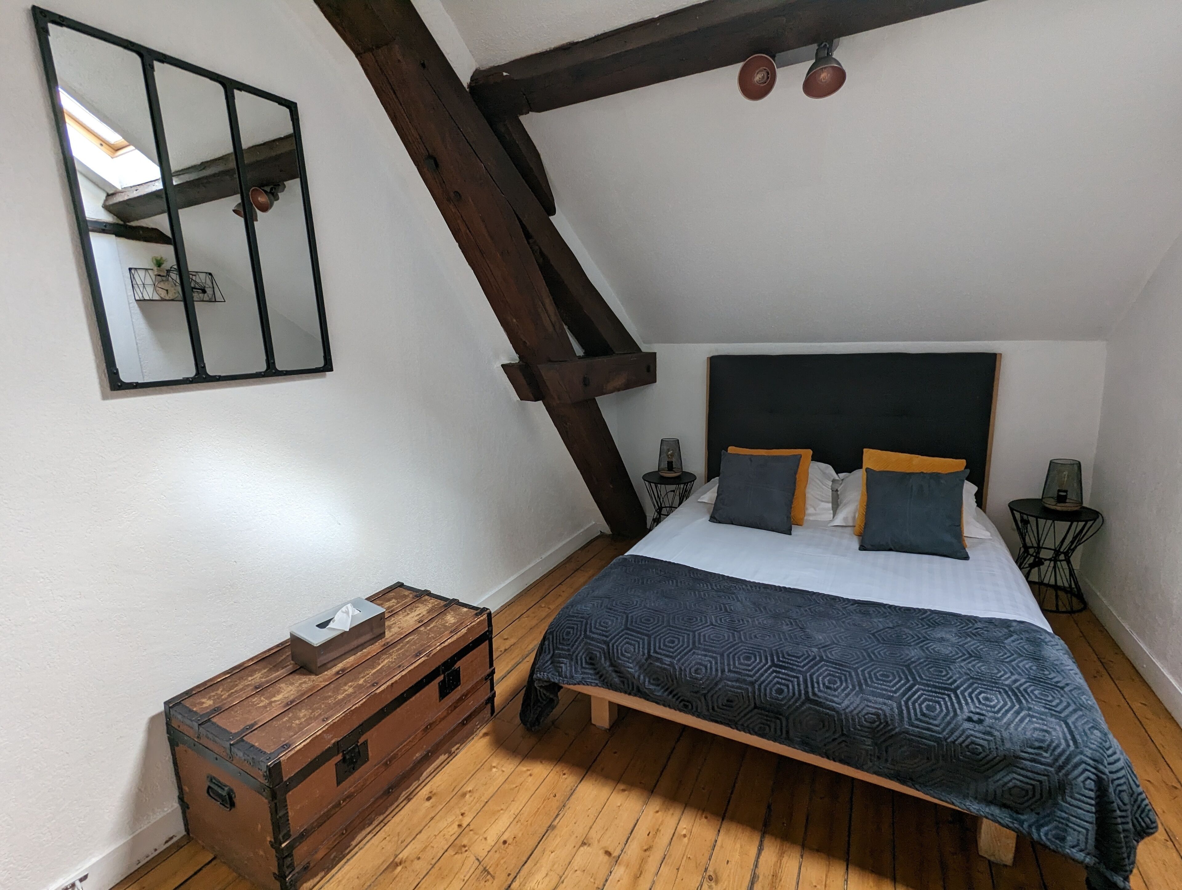 Un dormitorio con techo inclinado, una cama con ropa de cama estampada, un aparador de madera y una mesita de noche con una lámpara.