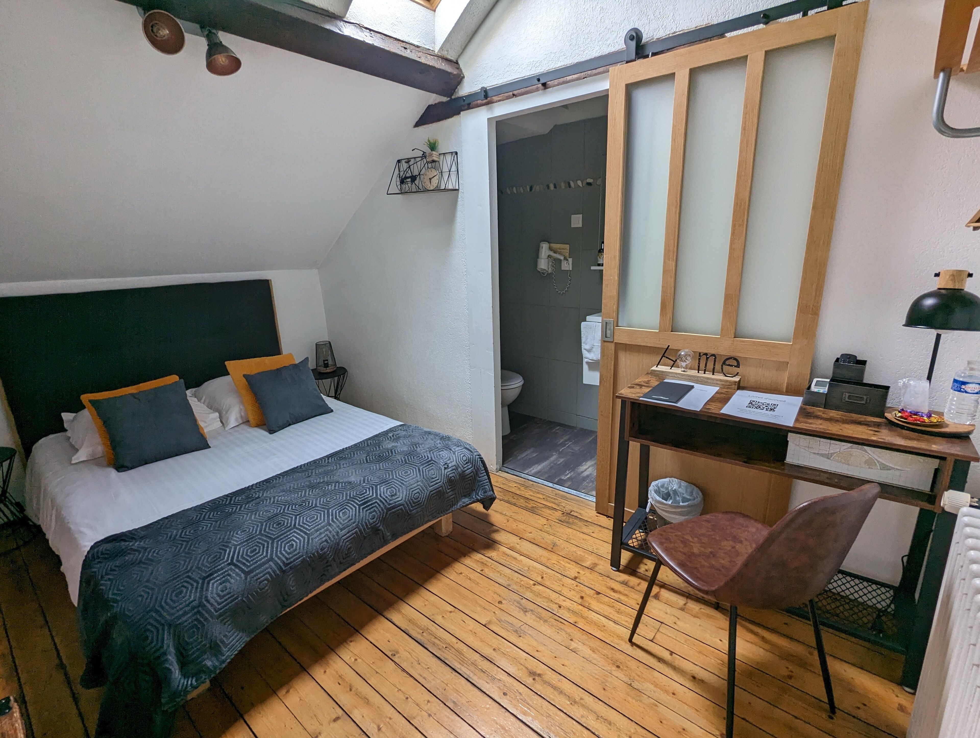 Une chambre à coucher avec un lit, un bureau et une chaise. Il y a une fenêtre au-dessus du lit et une porte qui donne sur une salle de bain.