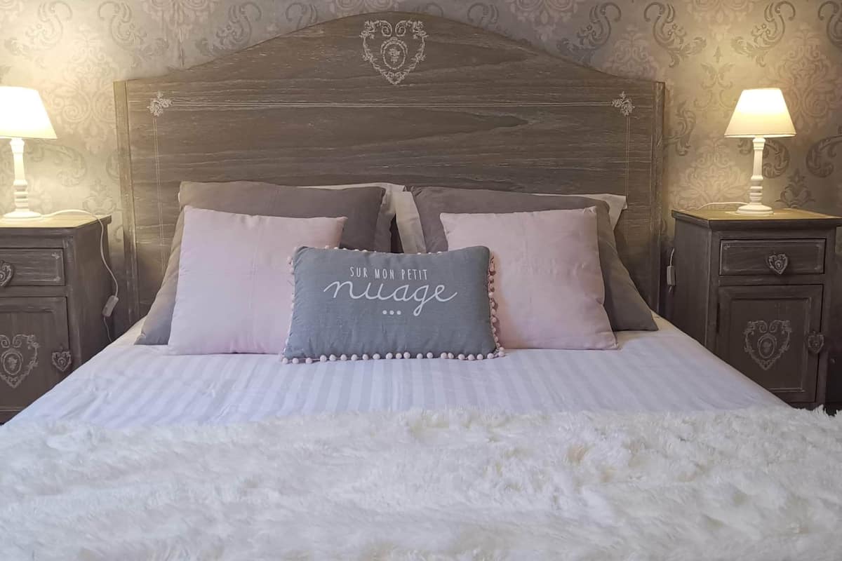 Un lit recouvert d’une couverture blanche et moelleuse, avec une tête de lit en bois foncé et deux tables de chevet dotées de lampes.