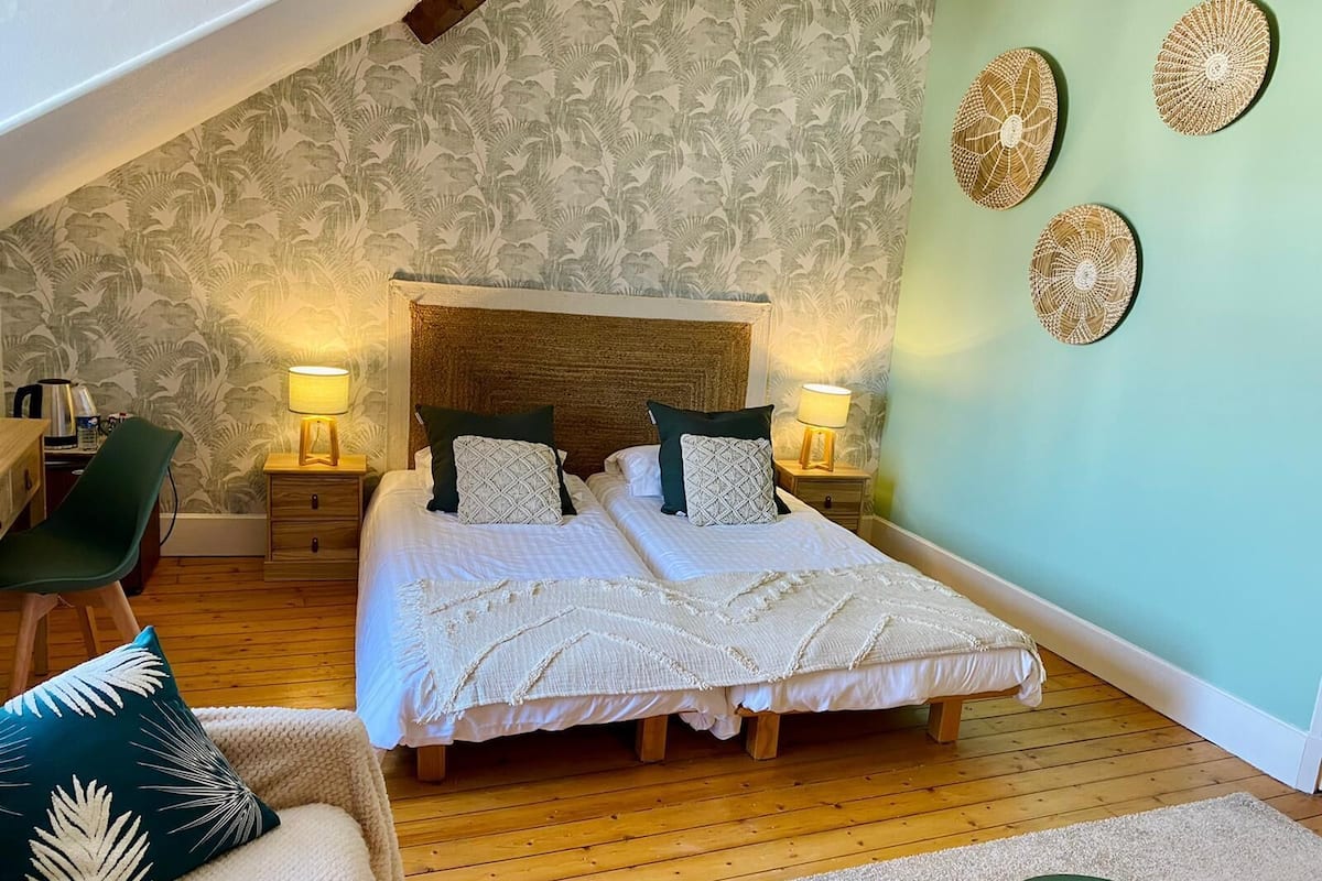 Une chambre confortable avec un grand lit, deux tables de chevet avec des lampes, un fauteuil vert et un plancher en bois.
