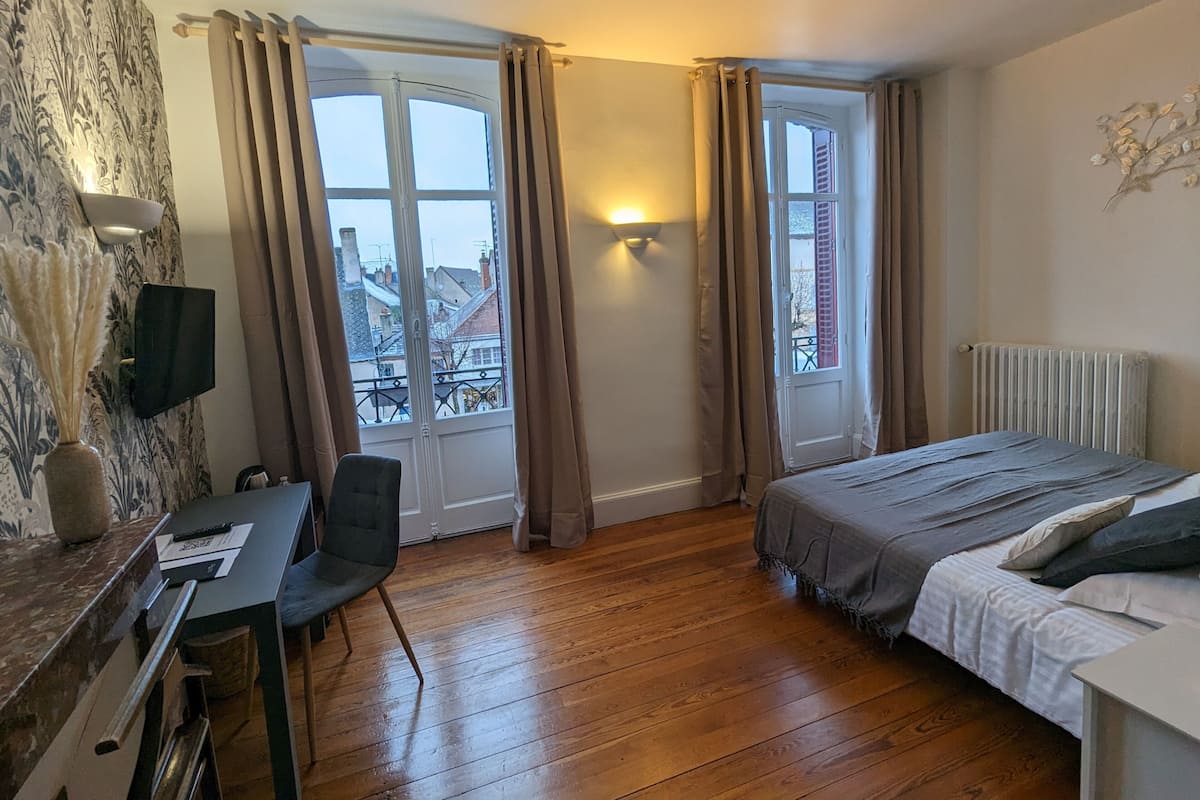 Une chambre à coucher comprenant un lit, un bureau, une chaise et deux fenêtres avec des rideaux.