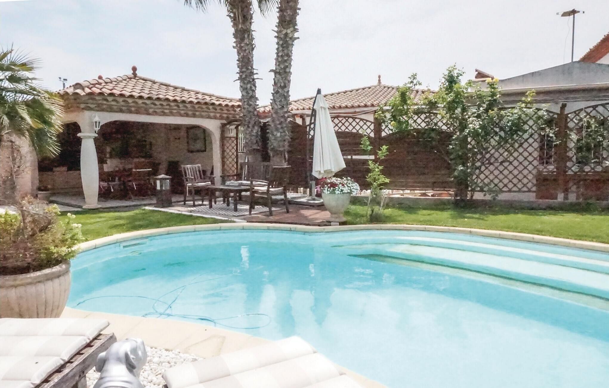 Une piscine entourée de chaises longues et de parasols, ainsi que d’un patio aménagé avec du mobilier d’extérieur et une pergola.